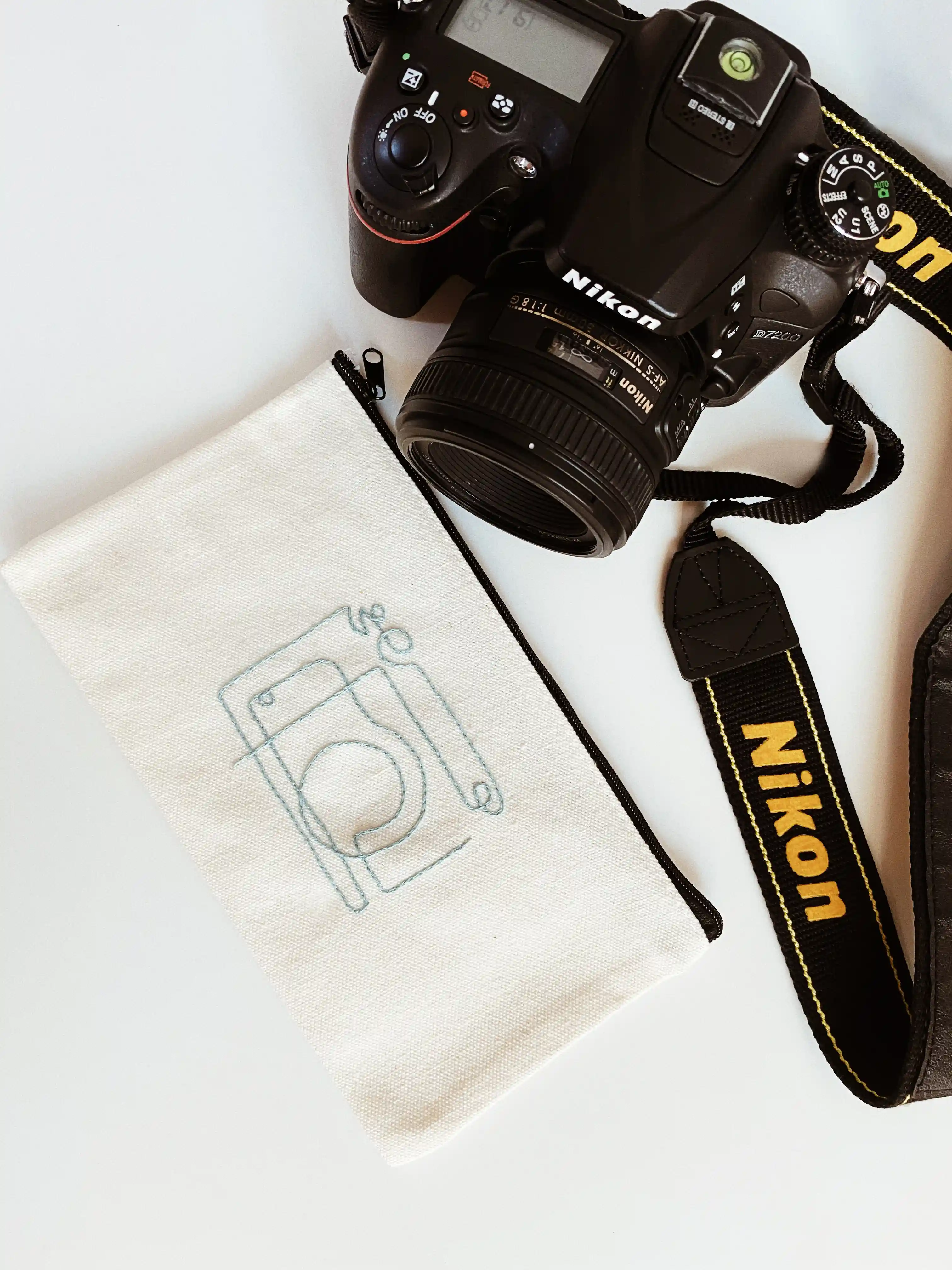 Linen pouch embroidered with a camera outline beside a Nikon camera