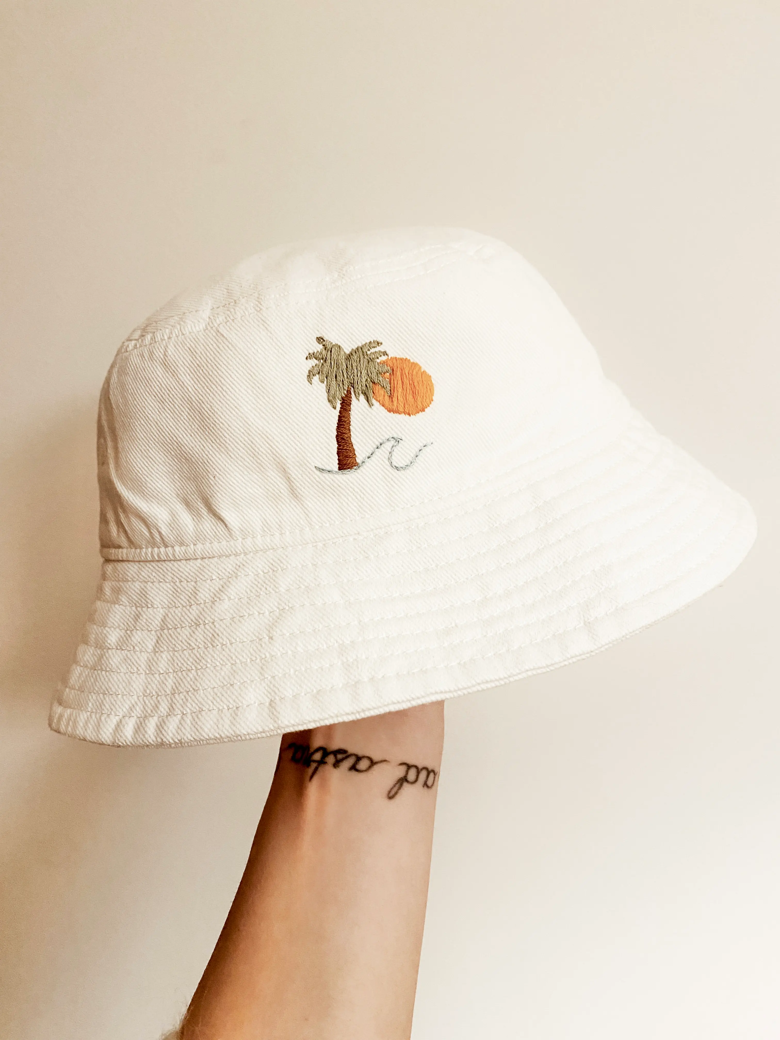 White bucket hat embroidered with a palm tree and sunset